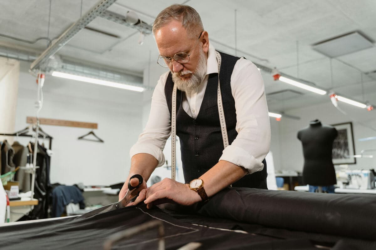 A tailor cutting dark fabric in his workshop