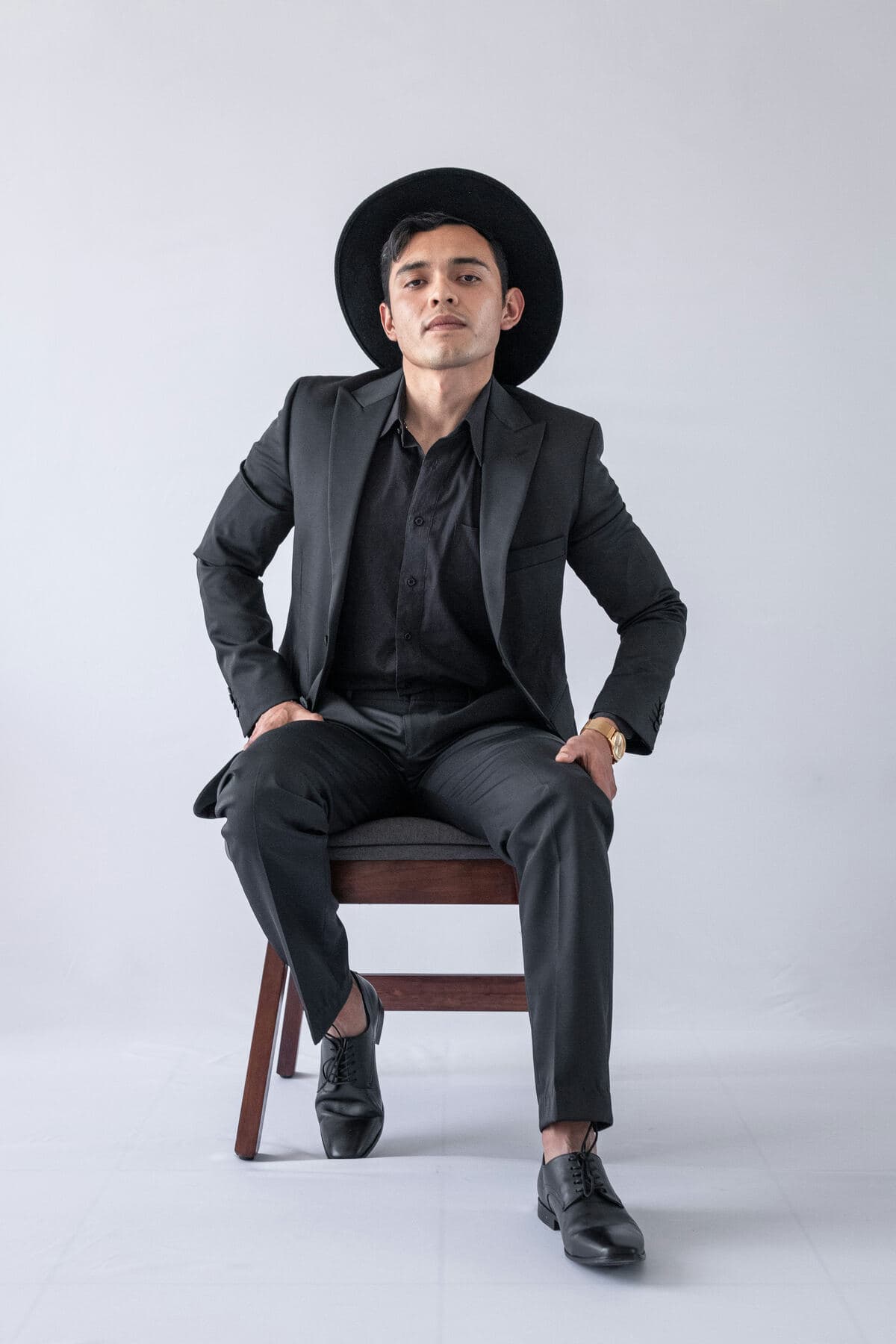 A designer in a dark suit and hat sitting on a chair
