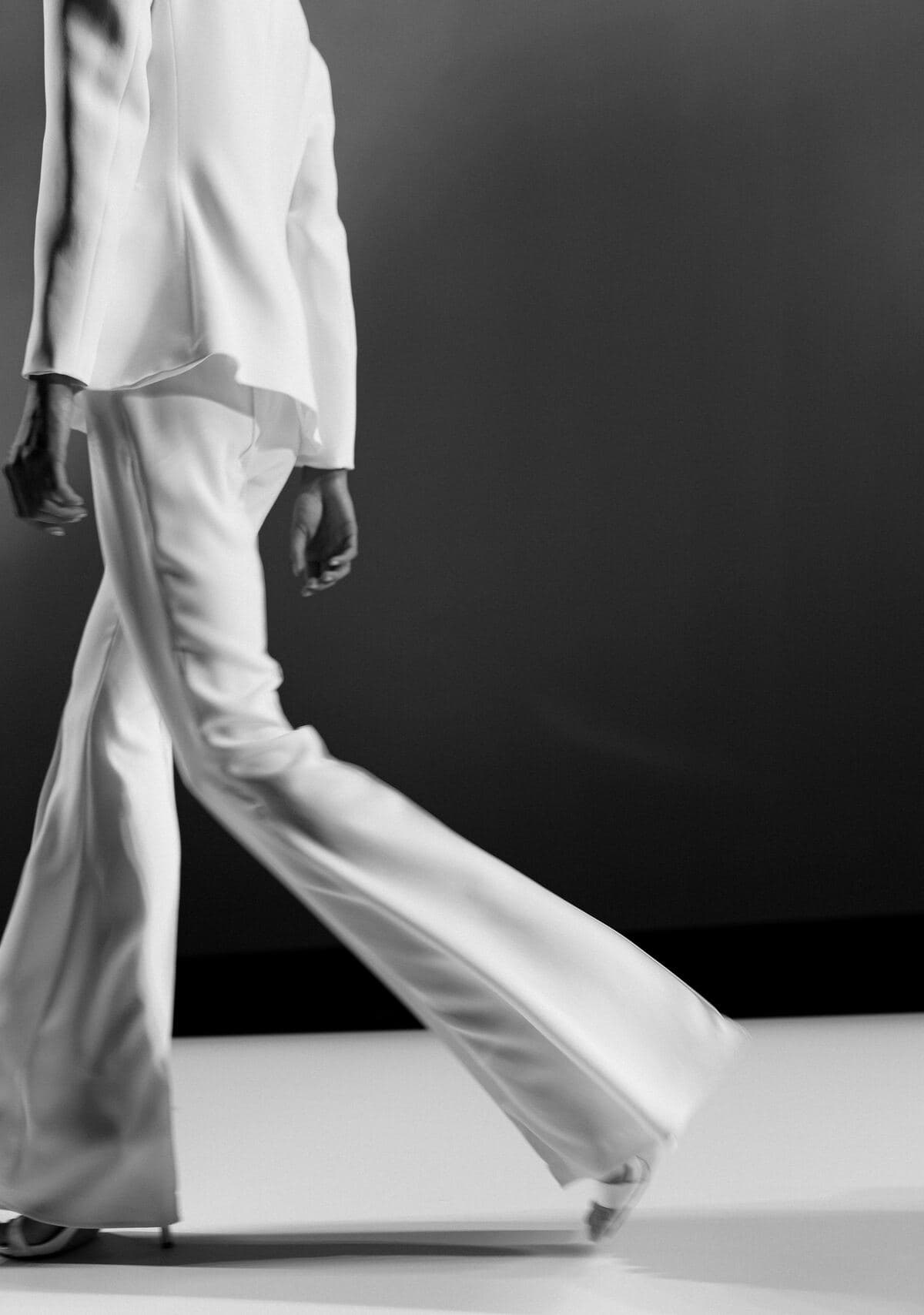 Black-and-white detail of a white suit with flared trousers, in motion