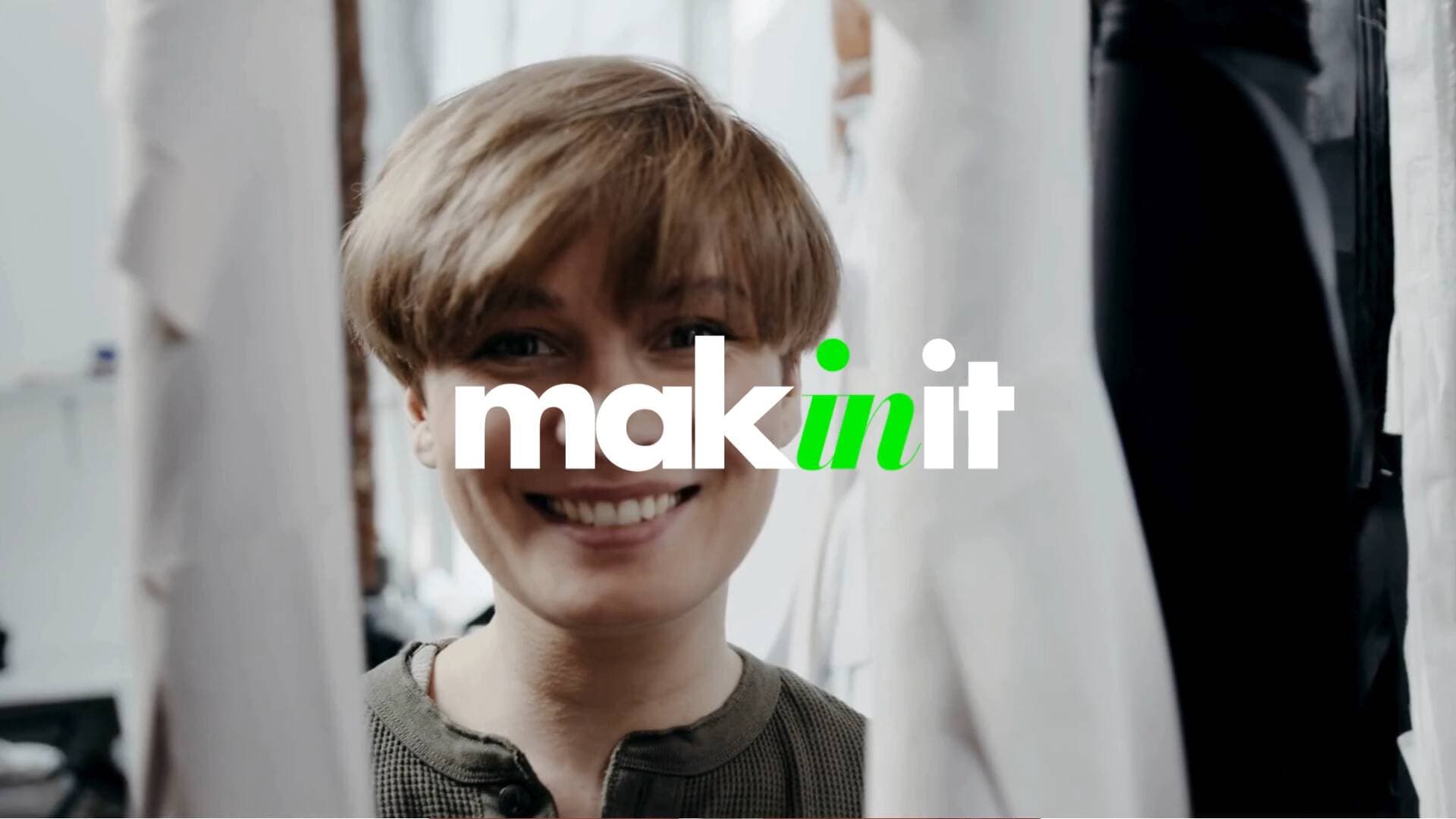 A person smiling in an atelier among hanging garments, with the MakinIt logo overlaid